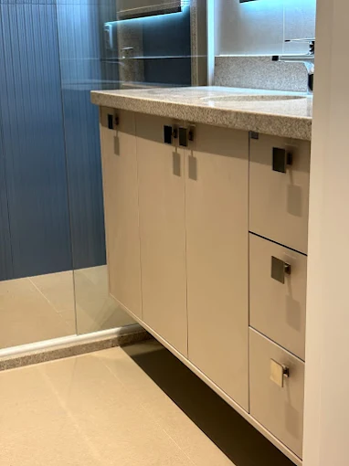 Gabinete de banheiro branco com portas e gavetas inferiores, bancada em granito cinza e revestimento azul