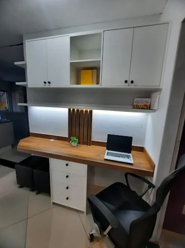 Home office compacto branco com armários superiores, bancada em madeira, iluminação LED e detalhe ripado