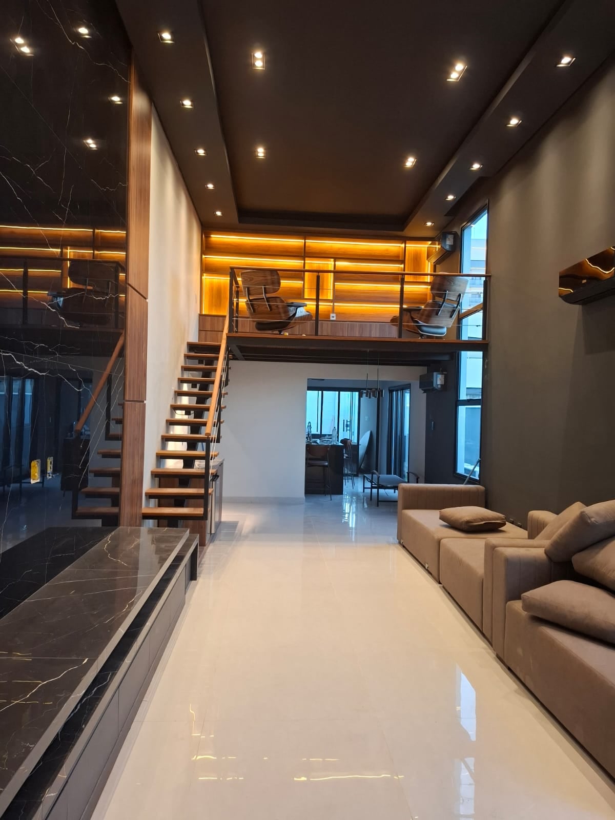 Sala de estar planejada em duplex com mezanino, escada suspensa e painel em mármore